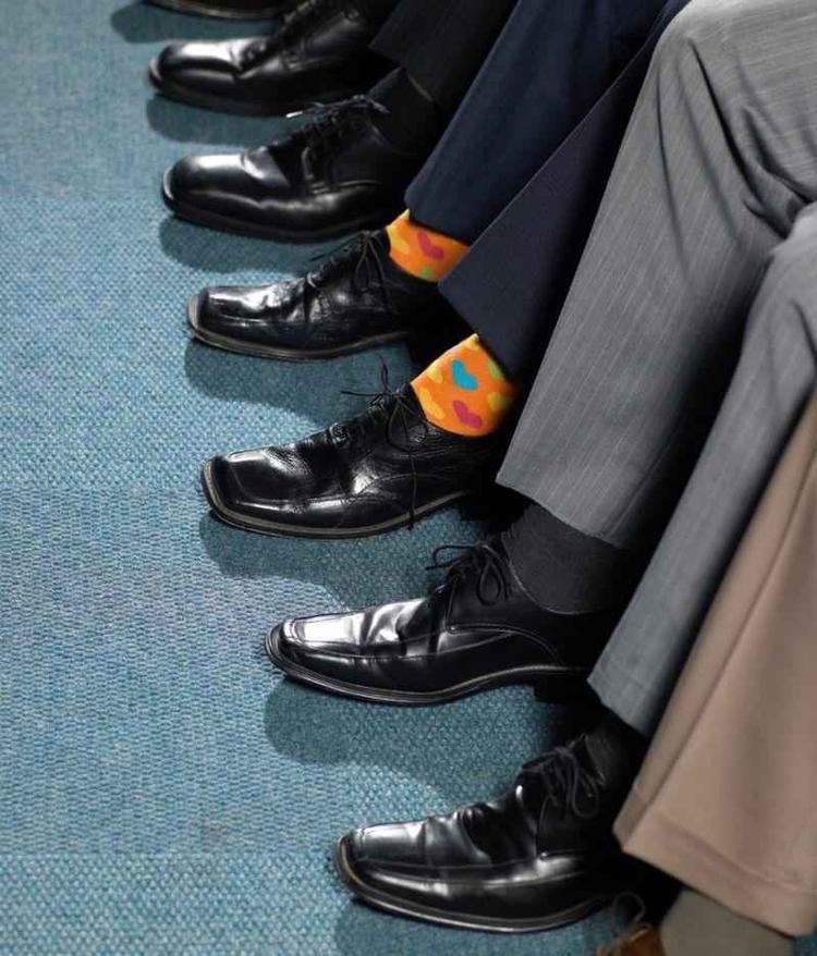 Ps de homens sentados, um deles se destacando com uma meia colorida