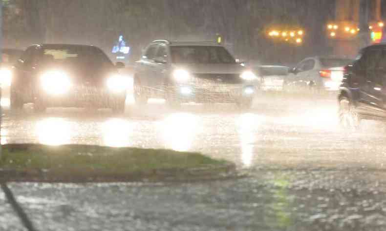 Carros com faris acessos, debaixo de chuva em BH