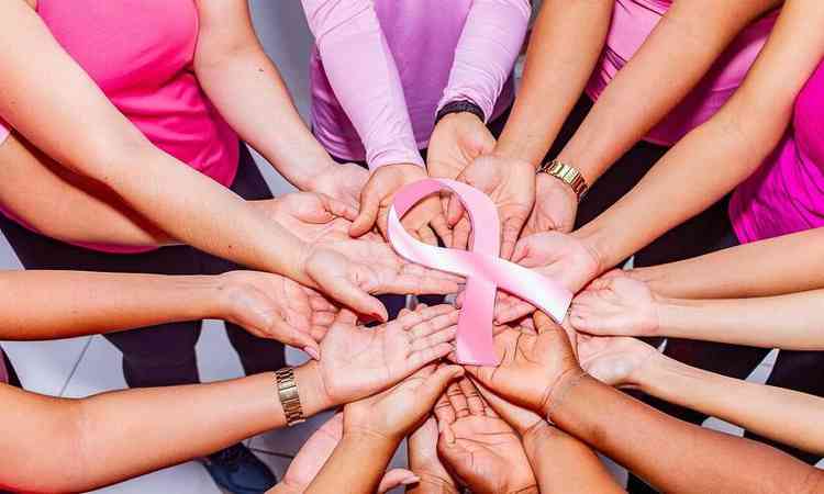 vrias mos de mulheres unidas em um centro, com camisas rosas e o lado rosa no centro da roda, smbolo do cncer de mama