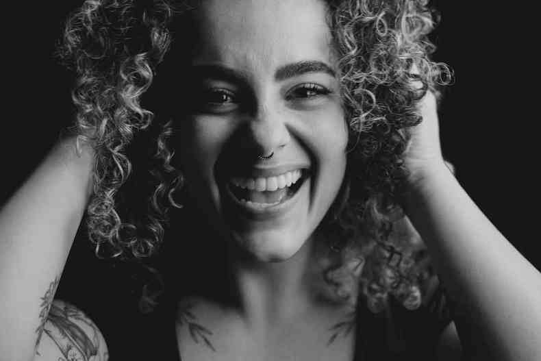 Cantora mineira Rayane Boldrini sorri, com as mos sobre os cabelos encaracolados