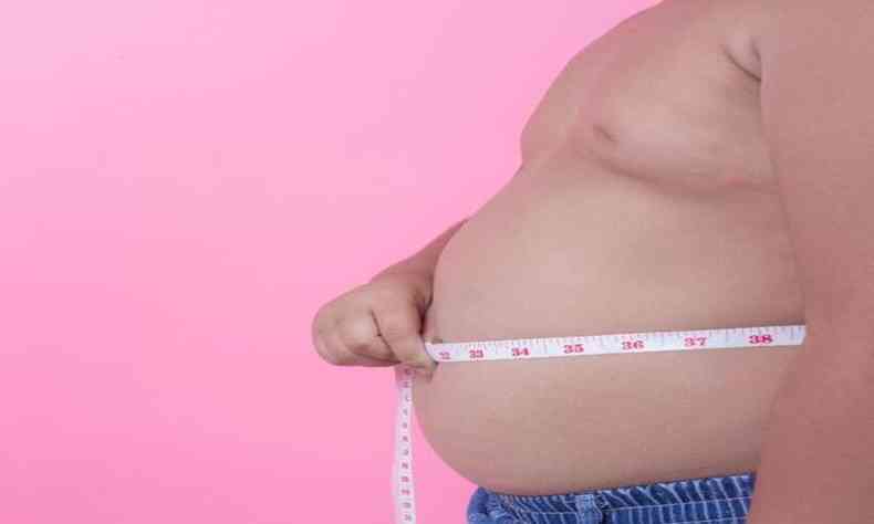Obeso medindo a barriga com uma fita métrica 