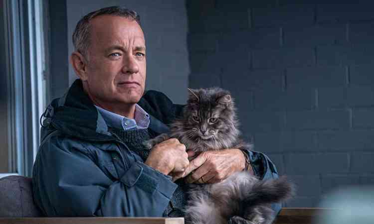 Tom Hanks olha para a frente, sentado com um gato no colo durante o filme O pior vizinho do mundo