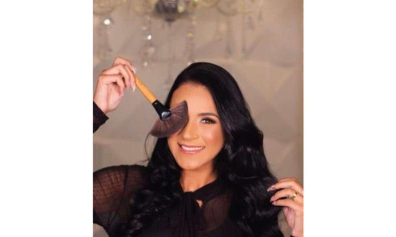 Maquiadora Gabriela Braga, uma mulher branca de cabelo medio preto, ela segura um pincel de maquiagem em frente ao seu rosto