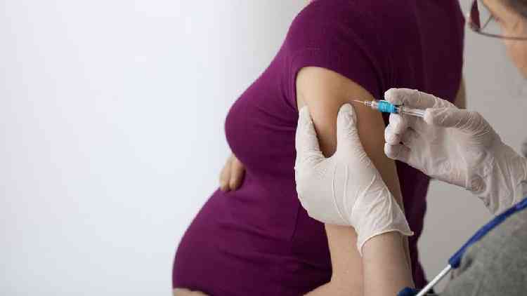 Enfermeira aplica vacina no brao de grvida; ambas esto de lado para a cmera