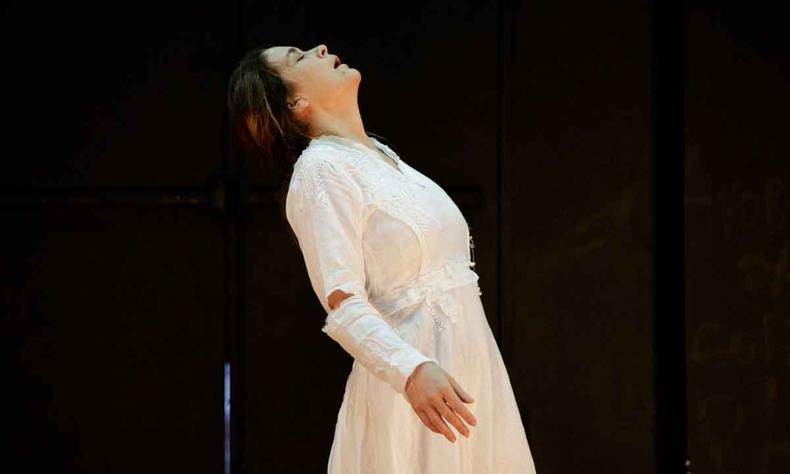 Com vestido branco, atriz Cludia Abreu flexiona o tronco para trs em cena de Virginia 
