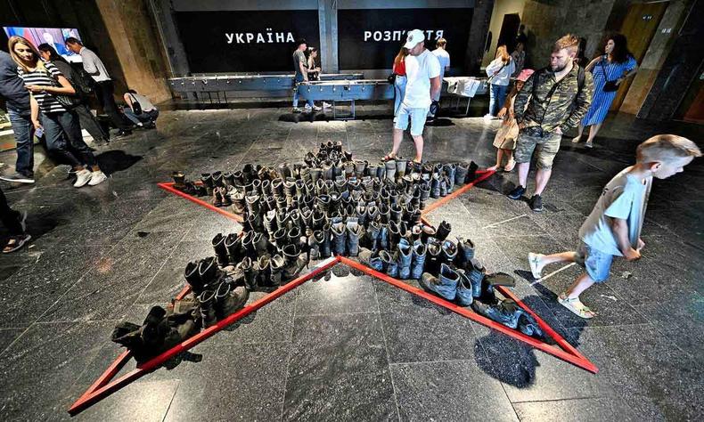 Em museu, pessoas observam estrela desenhada no cho. Dentro dela h botas de combatentes na Guerra da Ucrnia