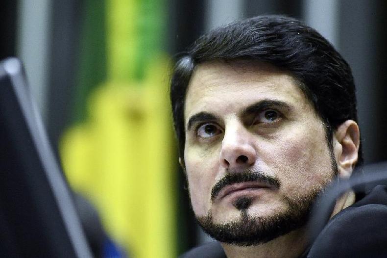 Retrato em close-up do senador Marcos do Val (Podemos-ES) no plenrio do Senado. Atrs, desfocada, a bandeira do Brasil. Do Val  um homem branco de cabelo e barba pretas.