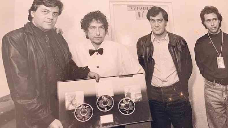 Em sua segunda visita ao Brasil, em 1991, Dylan posa ao lado de Sérgio Lopes, da gravadora Sony Music; e de Luiz Oscar Niemeyer e Paulo Rosa, da produtora Mills & Niemeyer, responsável por trazer o cantor ao Brasil