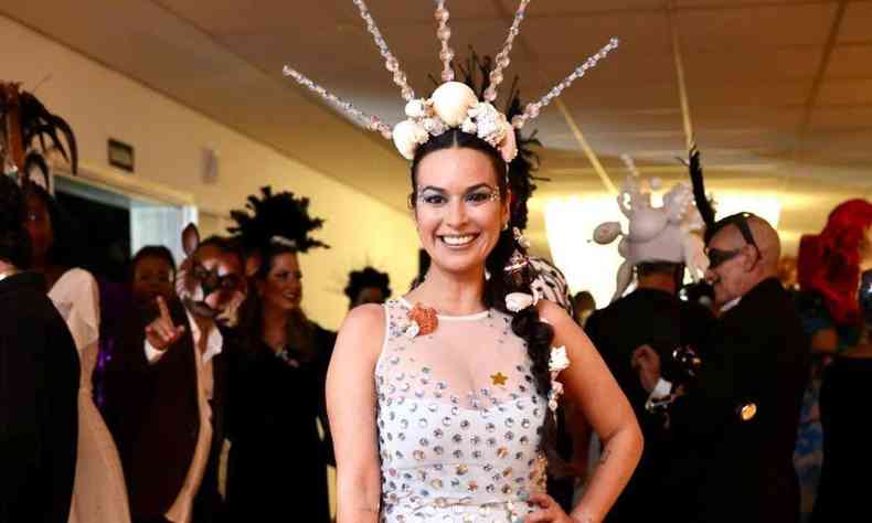 Usando vestido branco com penas, Chris Coelho sorri para a cmera durante baile de carnaval
