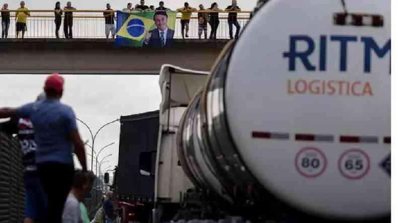 Estrada bloqueada em Jacare (SP); ao fundo, em passarela, apoiadores do presidente seguram bandeira com foto de Bolsonaro
