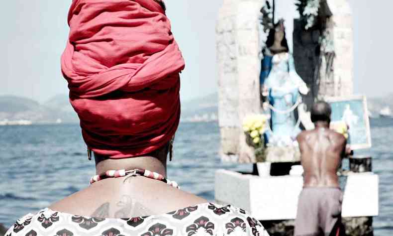 Mulher com turbante vermelho na cabea observa homem depositar oferendas a Iemanj 
