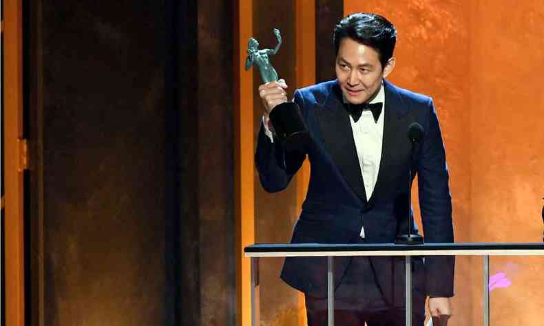de terno e gravata borboleta, ator Lee Jung-jae ergue o SAG Award e pende a cabea em agradecimento