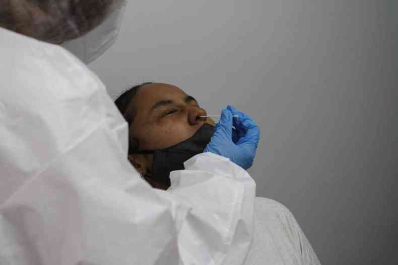 Homem sendo testado com cotonete no nariz. Enfermeira manuseia teste com luvas azuis