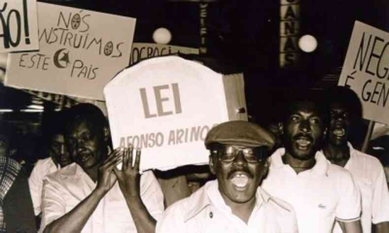 Foto antiga de homens negros manifestando com cartazes referentes  lei Afonso Arinos