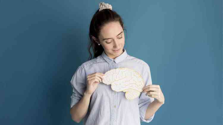 Mulher branco do cabelo preto, lao no cabelo e blusa azul segurando o desenho de um crebro