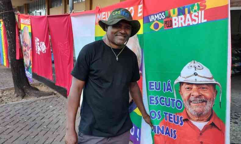 Homem sorri diante de varal de bandeiras do Lula