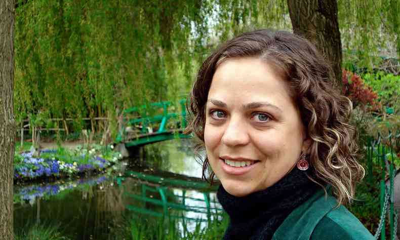 Clarissa Menicucci sorri num bosque com lago 