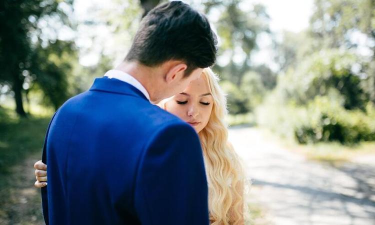 homem de terno azul, de costas, olhando para adolescente loira, de vestido branco, casando