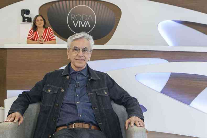 Caetano Veloso sorri, tendo ao fundo entrevistadora do programa de TV ''Roda viva''