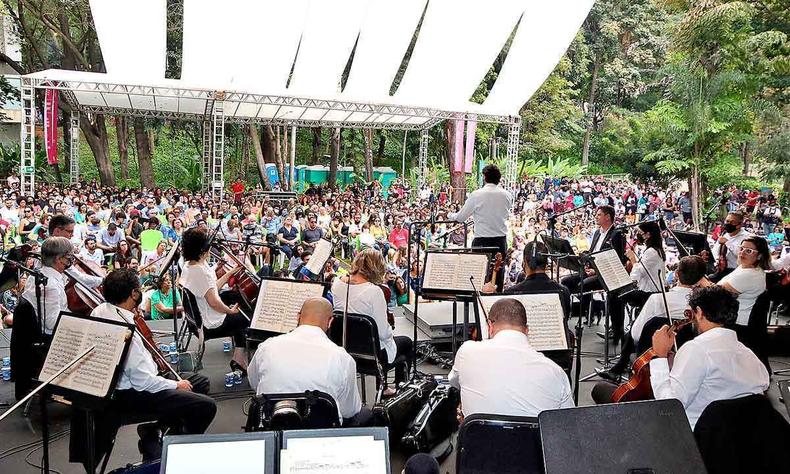 Vestidos de branco, msicos da Sinfnica de Minas Gerais tocam em palco armado ao ar livre no parque municipal