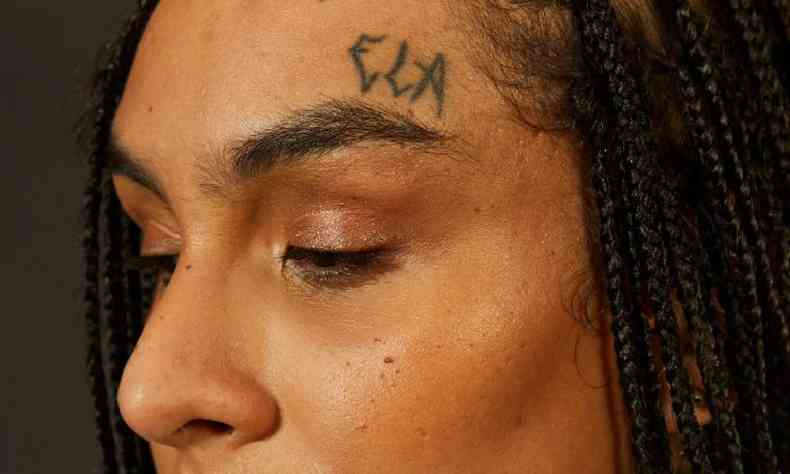 Perfil de Linn da Quebrada com foco em sua tatuagem, que diz 'ela'.