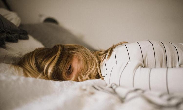 mulher deitada na cama, de barriga para baixo e olhos abertos