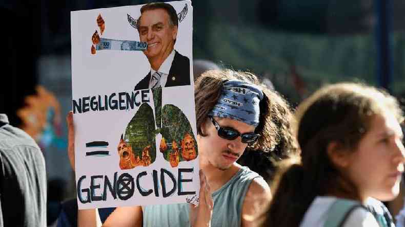 Em Londres, ativista segura cartaz com foto de Bolsonaro e de florestas em chamas, com as palavras 'negligncia' e 'genocdio' em ingls