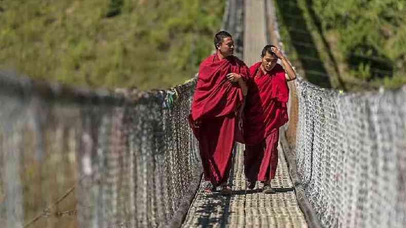 Dois monges budistas caminhando em uma ponte suspensa