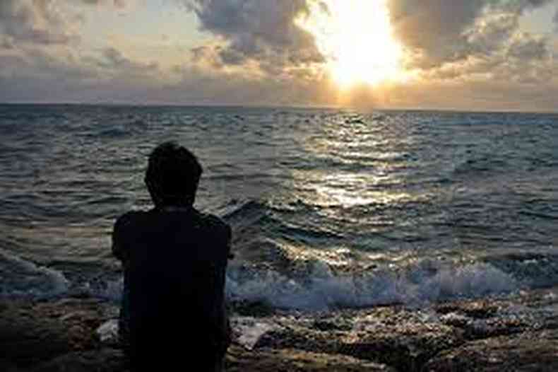 Homem sentado em frente ao mar no pr do sol