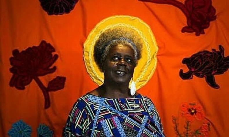 Conceio Evaristo posa na frente de um painel que coloca o sol atrs de sua cabea, como se fosse uma coroa. Ela  uma mulher negra de cabelos curtos, crespos e grisalhos.