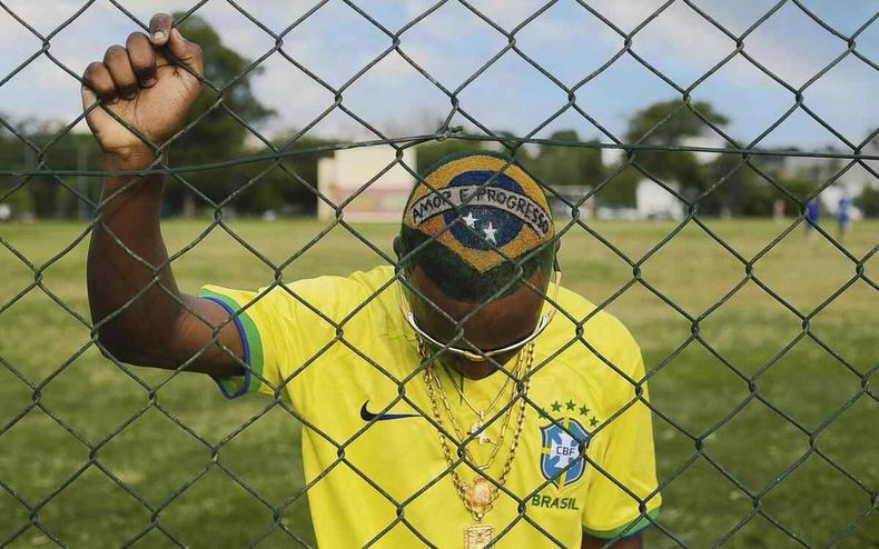 Jovem negro atrs de uma tela de alambrado, usando a camisa da seleo e com a bandeira pintada nos cabelos