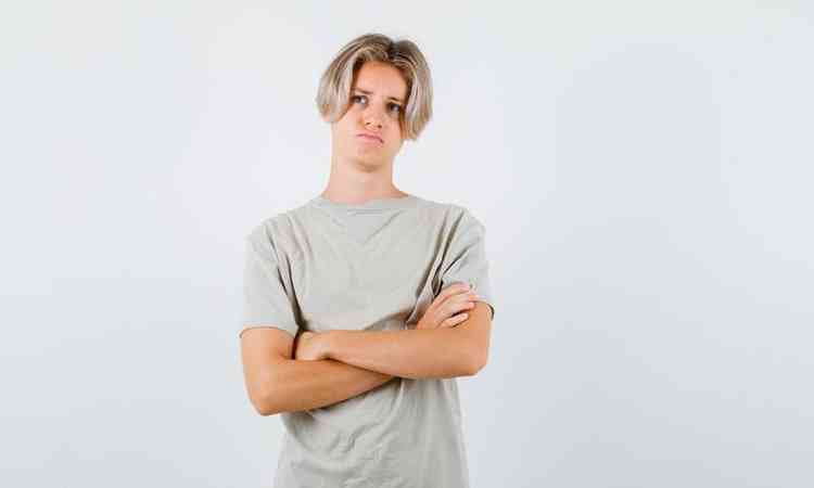 Jovem rapaz adolescente em p com os braos cruzados, olhando para cima em uma camiseta e parecendo desesperado. vista frontal.
