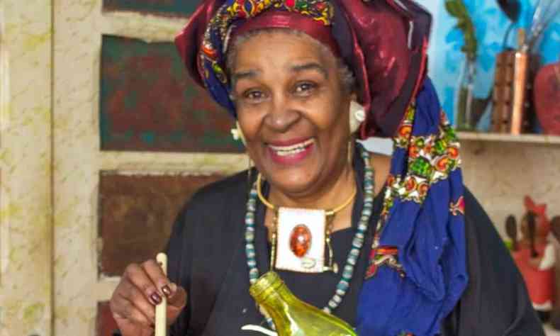 Zora Santos, uma mulher negra de 69 anos, usando turbante azul e vermelho sorrindo para a cmera