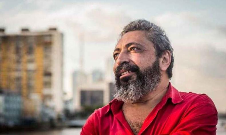 Escritor cearense Sidney Rocha, de camisa vermelha, aparece de lado, olhando para cima. Ao fundo, veem-se o cu e prdios em imagem desfocada