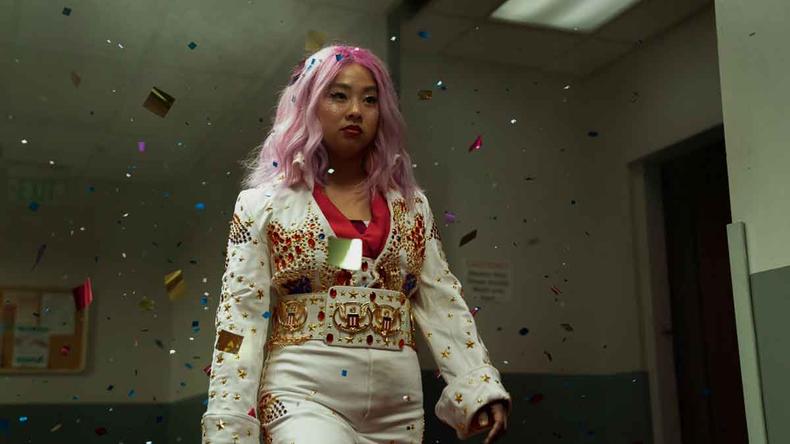De cabelo cor-de-rosa e macaco branco bordado com pedras, atriz Stephanie Hsu caminha, tendo o semblante desafiador