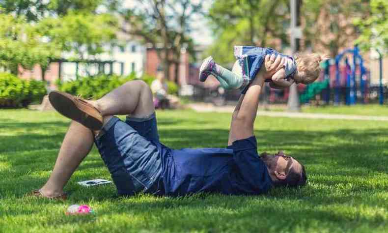 pai brinca com filha no parque, deitados na grama