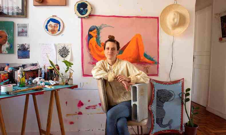 Mag Magrela sentada em cadeira apoiada em tijolo em seu atelier, decorado com objetos de arte