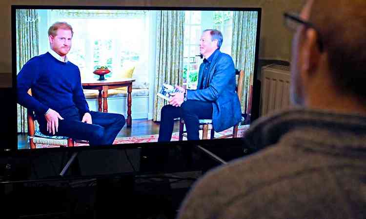 Homem, de costas, assiste na TV  entrevista do prncipe Harry ao apresentador Tom Bradby
