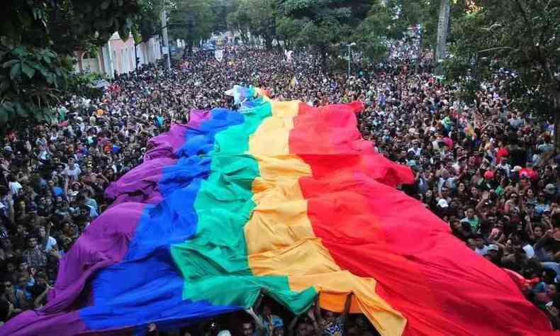 Foto tirada na Parada do Orgulho LGBT de Belo Horizonte em 2018. H uma multido nas ruas segurando uma imensa bandeira LGBT (com as cores do arco-ris) conjuntamente.