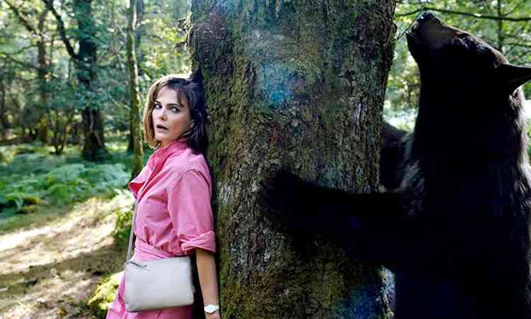 Atriz Keri Russell com rosto apavorado est encostada em rvore, do outro lado est urso negro, em cena do filme O urso do p branco
