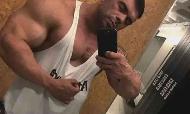 O fisiculturista Weldrin Lopes de Alcantara tira foto em frente ao espelho. Ele aparece de frente, flexionando um dos bceps e veste uma camiseta branca. 