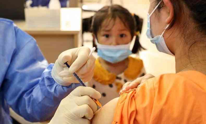 Menina observa mulher recebendo dose de vacina contra COVID-19(foto: STR / AFP)