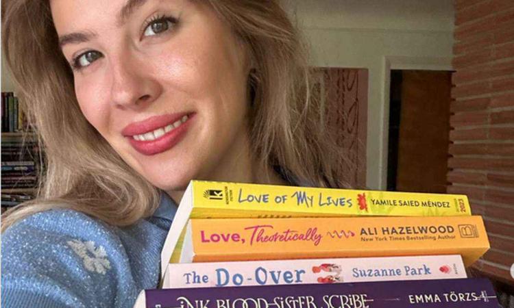 Escritora Emily Henry sorri e segura pilha de livros
