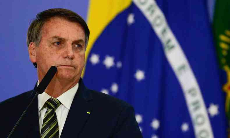 Bolsonaro em foto de quando ainda era presidente, com uma bandeira do Brasil ao fundo