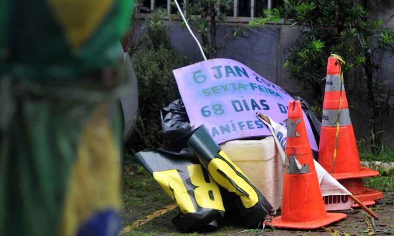 A imagem mostra a bandeira do brasil em primeiro plano com cones no fundo e um cartaz escrito com a contagem dos dias de manifestao