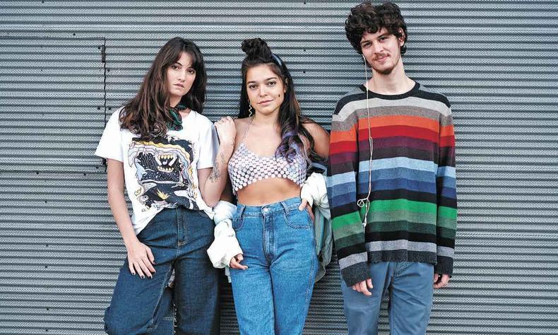 Os atores Elen Clarice, Bella Camero e Joo Oliveira, de p, com roupas jovens, encostados em porta metlica 