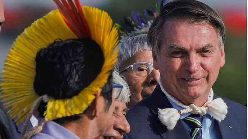 Bolsonaro fala sorrindo, ao lado de indígenas