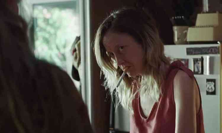 Atriz Andrea Riseborough com o cigarro na boca tem a cabea baixa e olha para o interlocutor, de costas, em cena do filme To Leslie