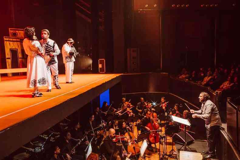 No fosso, Rodrigo Toffolo rege Orquestra Ouro Preto enquanto cantores e atores apresentam a pera Auto da compadecida no palco, em frente a ele
