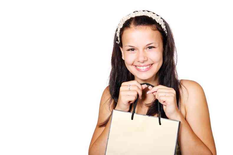 Moça sorri com sacola de compras nas mãos